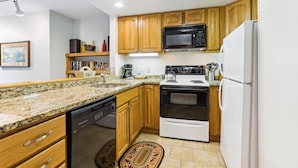 A compact kitchen with wooden cabinets, a black microwave, a white refrigerator, and a dishwasher. - 2-bedroom 2-bath condo with pool, hot tub, and private sauna. (Killington)