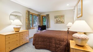 A bedroom with a large bed, two bedside tables with lamps, a dresser, a television, and a window with curtains. - 2-bedroom 2-bath condo with pool, hot tub, and private sauna. (Killington)