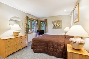 Quarto com uma cama grande, duas mesas de cabeceira com abajures, cômoda, televisão e uma janela com cortinas.
