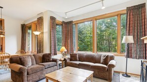 A cozy living room with a brown sofa set, a wooden coffee table, and large windows with curtains. - Charming Highridge Condo F2: Access to Pool, Hot Tub, and More! (Killington)