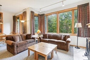 Relax in a spacious living room with a comfortable sofa set, dining area, and large windows offering a view of the surrounding landscape.