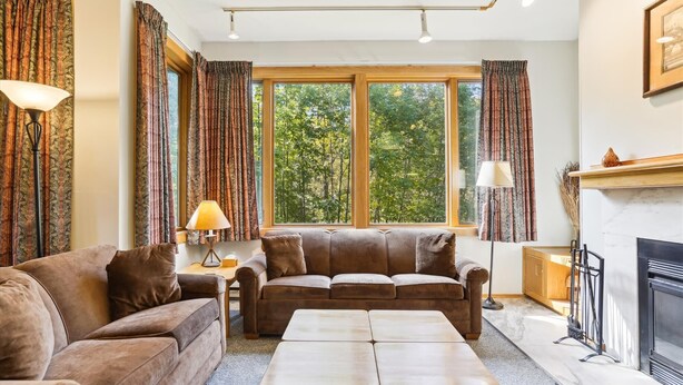 A cozy living room with a brown leather sofa, a wooden coffee table, and a fireplace. - 2-bedroom 2-bath condo with pool, hot tub, and private sauna. (Killington)