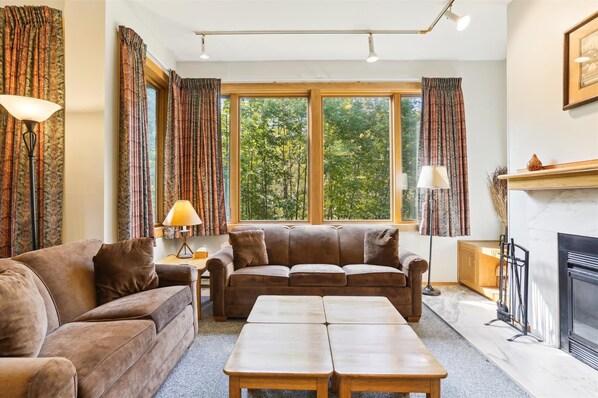 A cozy living room with a brown leather sofa, a wooden coffee table, and a fireplace. - 2-bedroom 2-bath condo with pool, hot tub, and private sauna. (Killington)