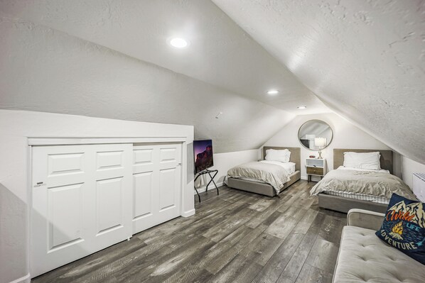 A bedroom with a loft-style ceiling, a large closet, two beds, a small table, and a mirror.