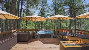 Een houten terras met buitenmeubilair, een jacuzzi en een vuurkorf.