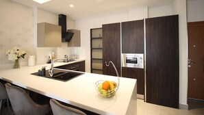 A modern kitchen with a central island, built-in oven, and dark wood cabinets. - Mirage Residences - 2 Bedroom Unit (Accra)