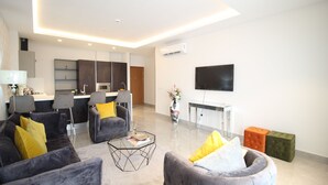 A modern living room with a sofa, armchairs, a coffee table, and a flat-screen TV mounted on the wall. - Mirage Residences - 2 Bedroom Unit (Accra)