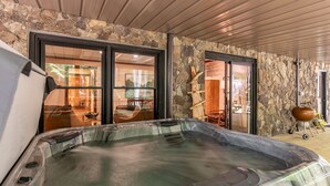 Un jacuzzi en una habitación con paredes de piedra y grandes puertas correderas de vidrio que dan a un comedor.