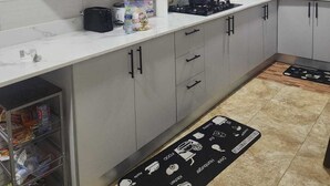 A modern kitchen with white cabinets, a black stove, and a window with decorative patterns. - Apartment Vacation Rental Accra Adenta  (MARLEJOR, Adenta Municipality)