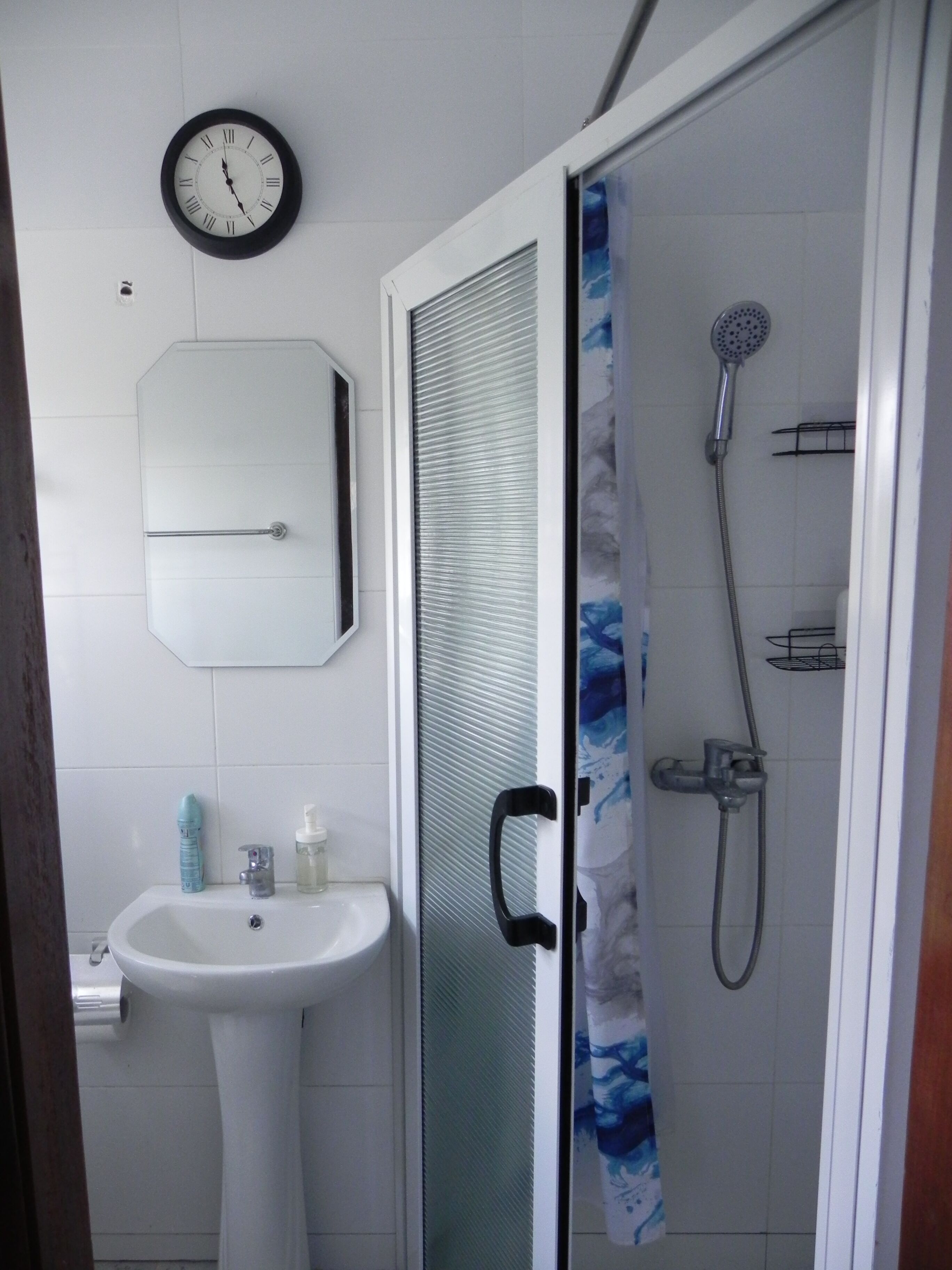 Ein Badezimmer mit Waschbecken, Toilette, Dusche und einer Wanduhr.