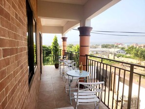 Ein Balkon mit weißen Stühlen und Tischen, einem Blumentopf und Blick auf eine Wohngegend.