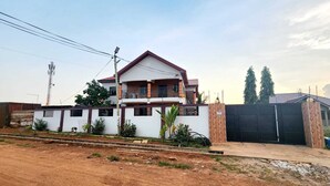 A two-story house with a balcony, a gated entrance, and a dirt driveway. - Apartment Vacation Rental Accra Adenta  (MARLEJOR, Adenta Municipality)