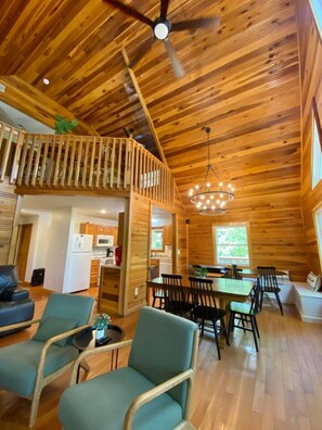 Un intérieur de cabine spacieux, avec un plafond haut, des murs en bois, un coin repas agrémenté d’un lustre, et un balcon doté d’une balustrade.