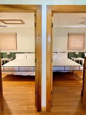 Une chambre aux murs recouverts de miroirs, avec deux lits, un plancher en bois et une tête de lit verte.