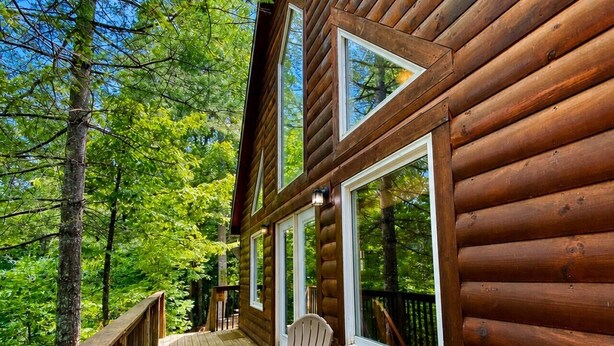 Uma cabana de madeira com varanda, duas cadeiras Adirondack e grandes janelas.