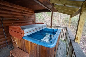 Une cabane en bois avec un jacuzzi situé sous un porche abrité.
