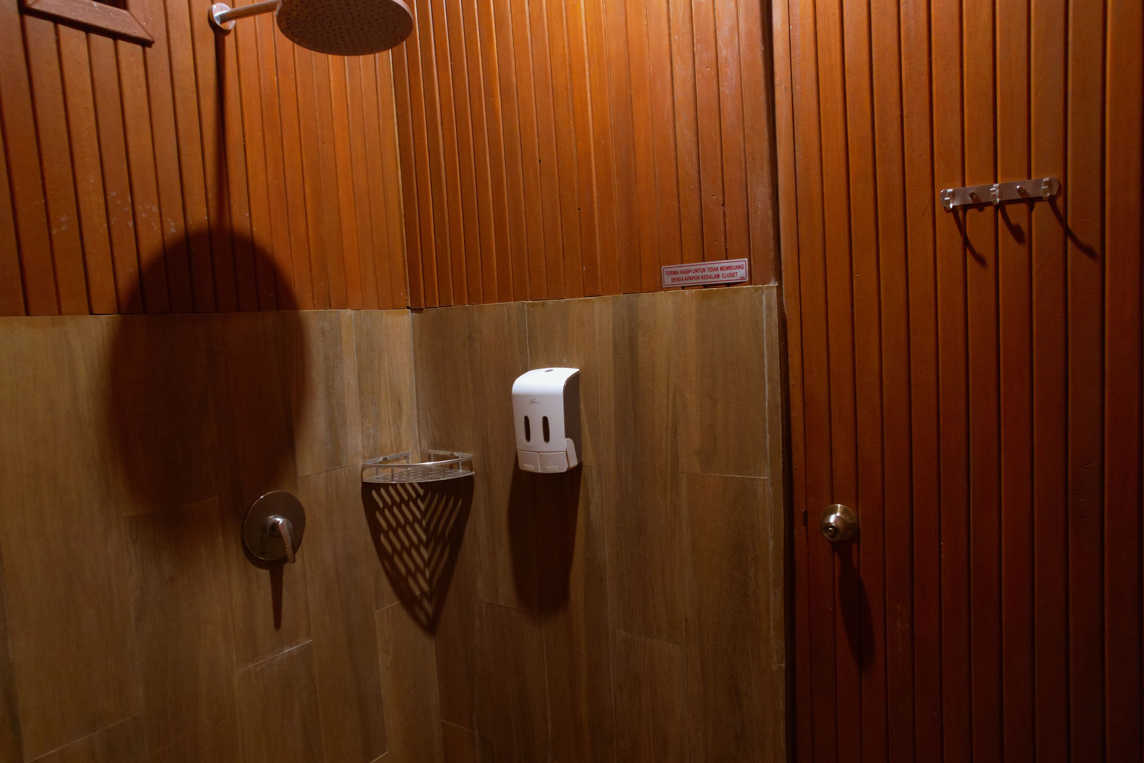 Un baño revestido de paneles de madera con ducha, secamanos y dispensador de toallas.