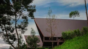 A modern building with a sloped roof, surrounded by lush greenery and trees. - KEMA Merbabu powered by Cocotel (Ampel)