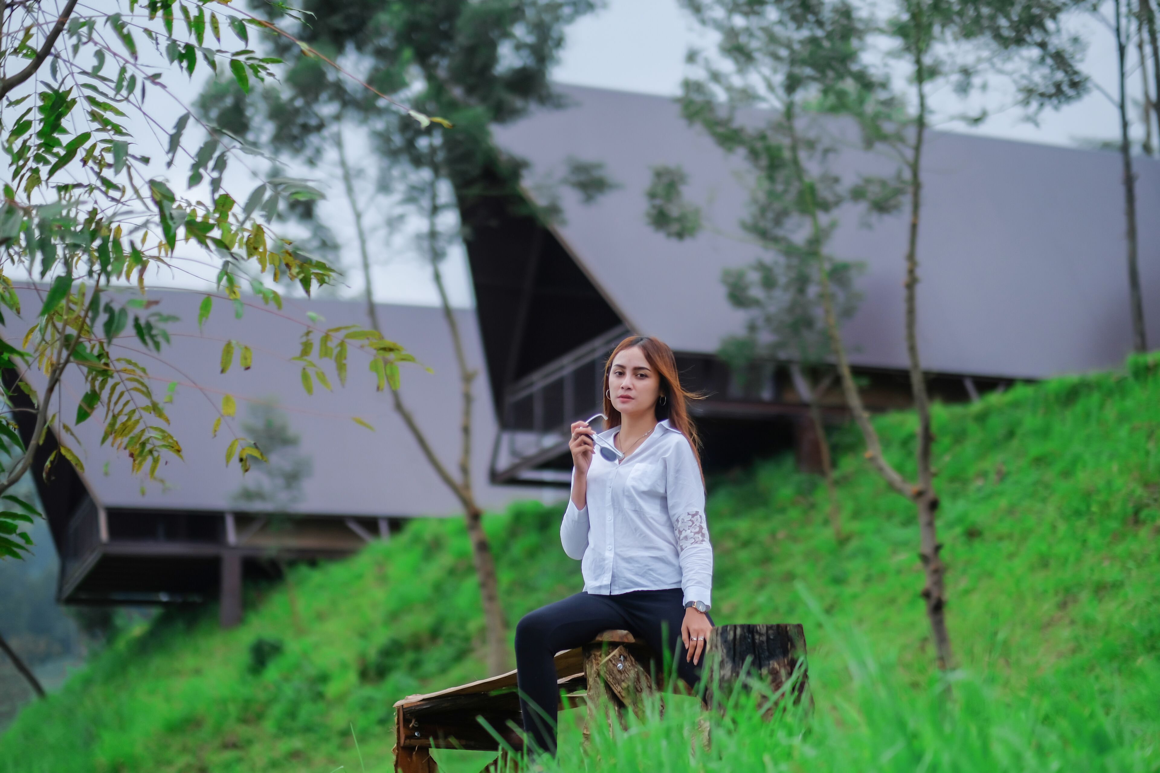 A person sitting on a bench in a natural setting with greenery and a modern building in the background.