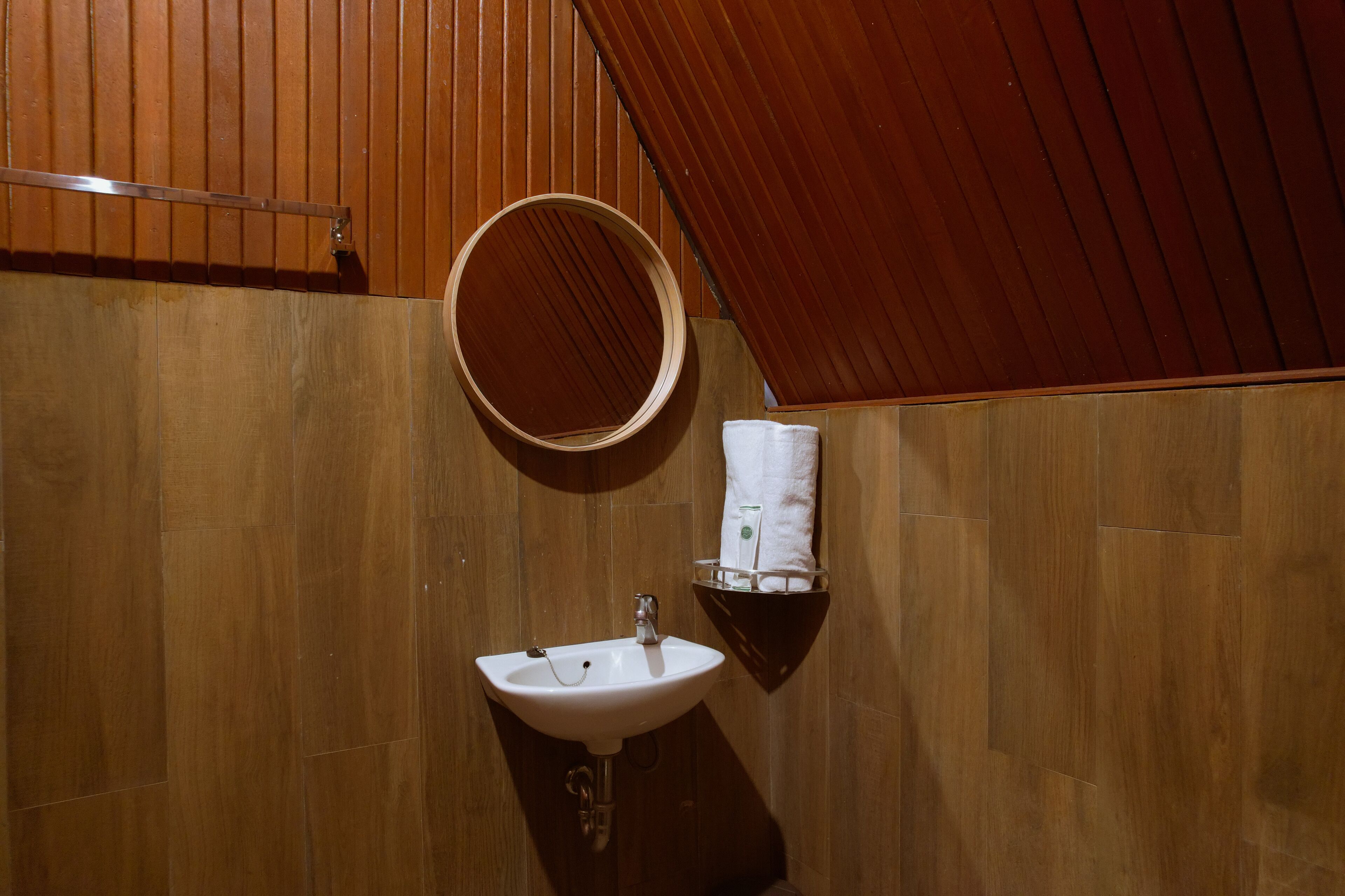 A bathroom with a wooden wall, a round mirror, a sink, and a towel rack.