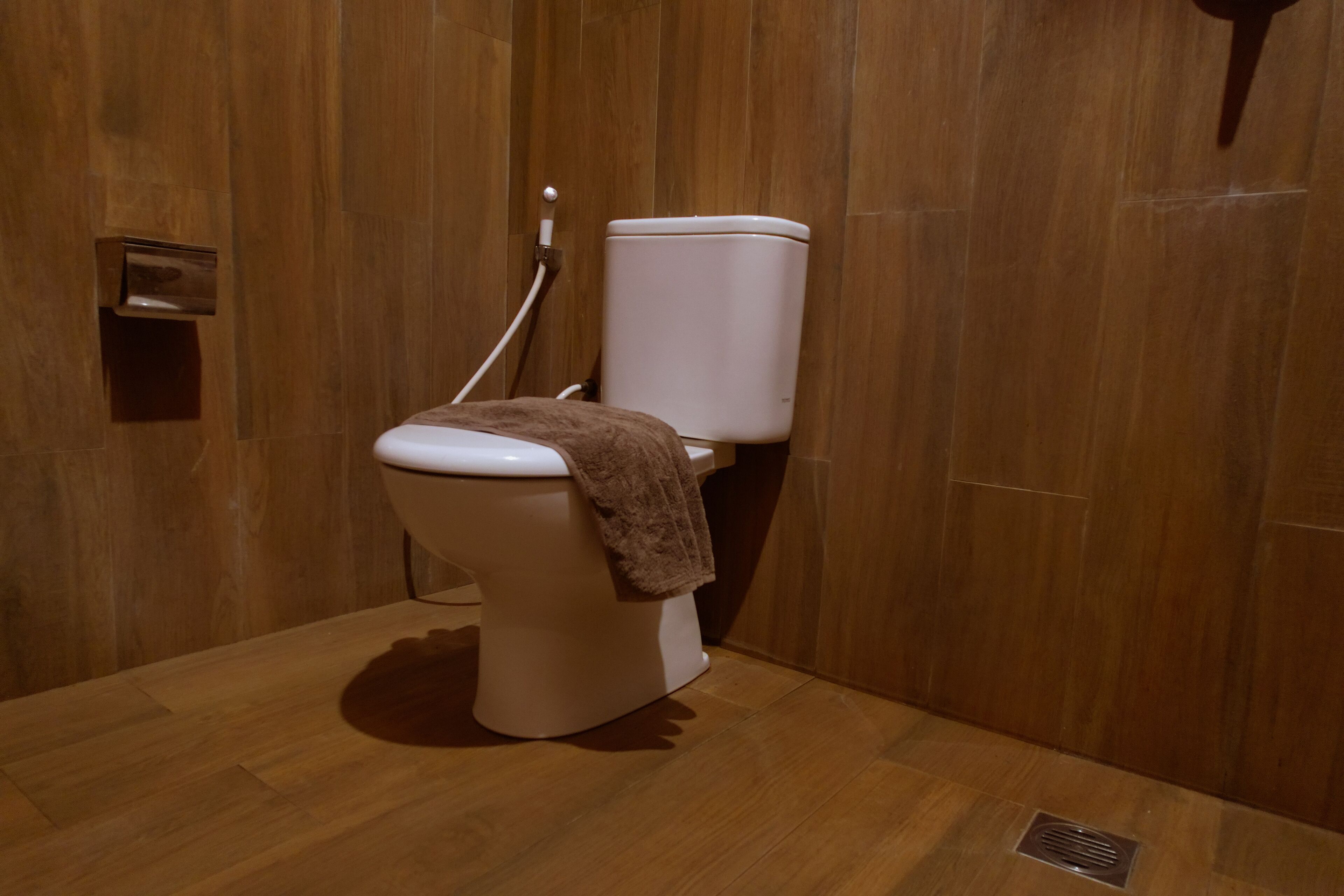 A modern bathroom with a wooden floor and walls, a white toilet, and a towel hanging on the seat.