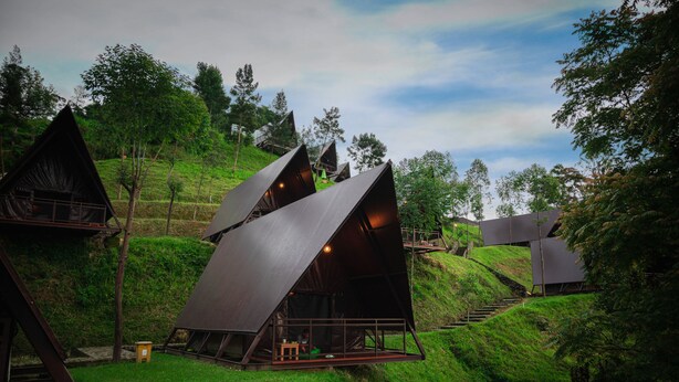 A series of triangular, modern cabins nestled in a lush, green hillside. - KEMA Merbabu powered by Cocotel (Ampel)