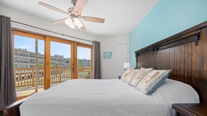 Une chambre dotée d’un grand lit, d’un ventilateur de plafond et offrant une vue sur une piscine et des bâtiments, grâce à une porte-fenêtre coulissante.