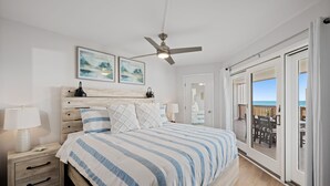 A bedroom with a bed, nightstands, a ceiling fan, and a view of the outdoors through a sliding door.