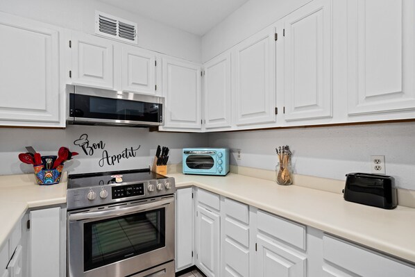 A kitchen with white cabinets, a stainless steel oven, a microwave, a toaster, and a decorative sign that reads "Bon Appetit".
