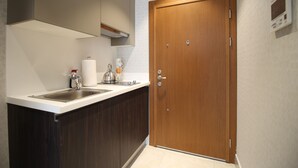 Una cocina moderna con armarios de madera oscura, encimera blanca, pileta de acero inoxidable y una puerta de madera con panel de control.