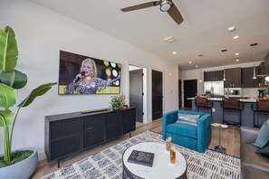 A modern living room with a flat-screen TV, a blue sofa, a coffee table, and a large plant. - Halcyon-Odyssey-Walk to Restaurants & bars! (Nashville)