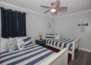 A bedroom with two beds, a ceiling fan, and nautical-themed decor.