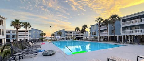 A swimming pool with lounge chairs and palm trees, surrounded by multi-story buildings.