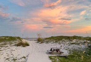 A sandy beach path leading to a wooden picnic table with a view of the ocean and a sunset sky. - Sea Oats H205 - Fall in Love with This Stunning Condo with Great Views! (Gulf Shores)