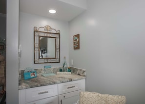A bathroom with a marble vanity, a large mirror with a decorative frame, a towel rack, and a sign on the wall. - Sea Oats H205 - Fall in Love with This Stunning Condo with Great Views! (Gulf Shores)