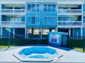 A two-story building with a pool area, including a hot tub and a sign with pool rules.