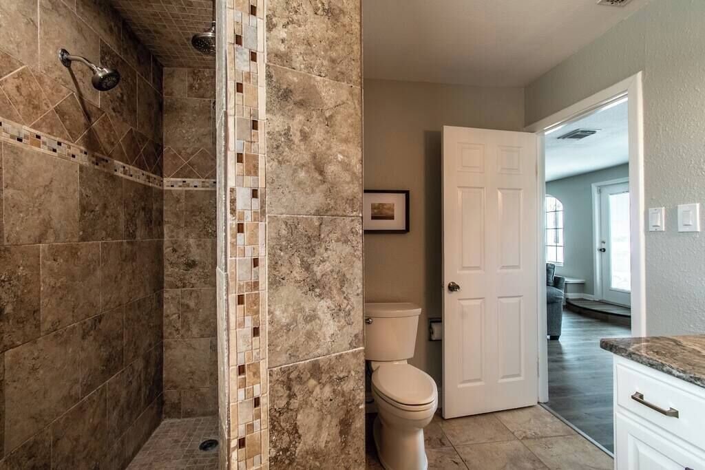 A bathroom with a shower, toilet, and a door leading to another room.
