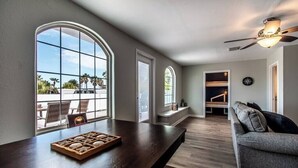 A spacious living area with large windows, a dark wooden table, and a grey sofa. - Sail Away! Your Coastal Pool Oasis Awaits (Corpus Christi)