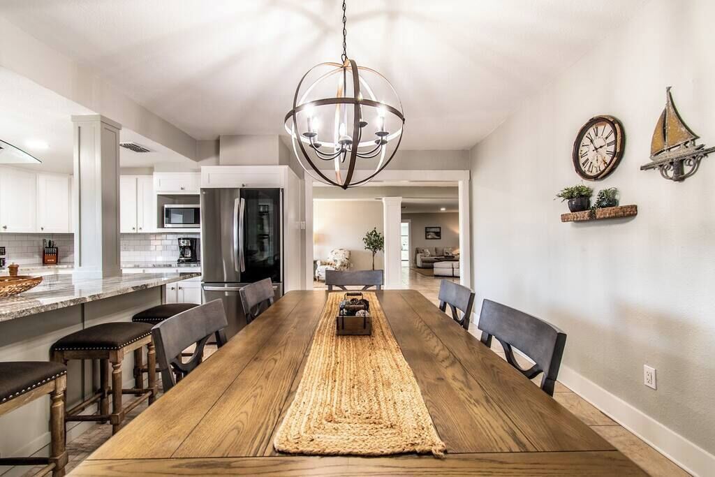 Uma sala de jantar com uma mesa de madeira, cadeiras, um tapete tecido e um lustre.