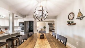 A dining area with a wooden table, chairs, a woven rug, and a chandelier. - Sail Away! Your Coastal Pool Oasis Awaits (Corpus Christi)