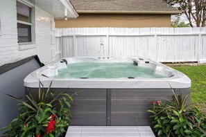 A hot tub in a backyard with a white fence and greenery around.