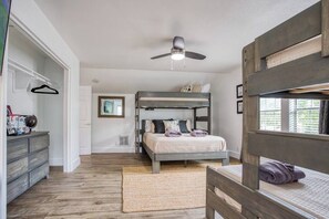 A bedroom with a bunk bed, a ceiling fan, a dresser, and a window with blinds.