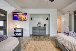 A bedroom with a bed, a TV mounted on the wall, a dresser, and a door leading to another room.