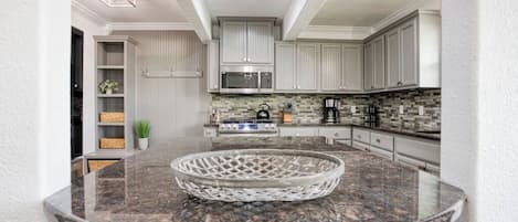 A modern kitchen with white cabinets, a granite countertop, and a microwave.