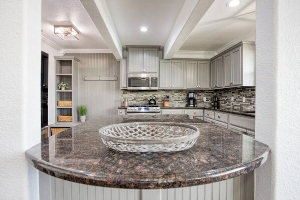 A modern kitchen with white cabinets, a granite countertop, and a microwave.
