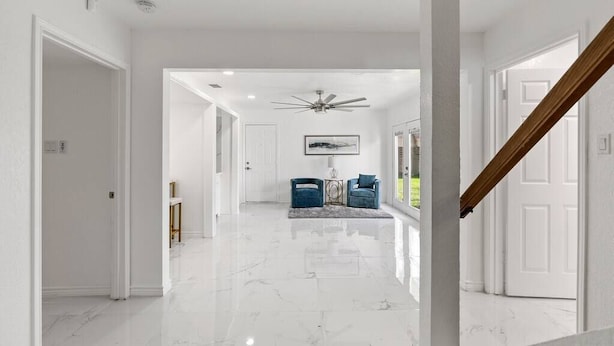 A spacious hallway with a marble floor leading to a seating area with two blue chairs and a small table. - Corpus Christi Gem (Corpus Christi)