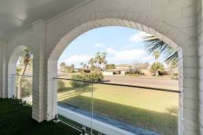 A covered outdoor area with white brick arches, a glass railing, and a view of a road and greenery. - Corpus Christi Gem (Corpus Christi)