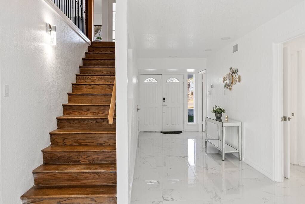 A staircase with wooden steps leading to a white interior space with a marble floor and a white console table with a plant.