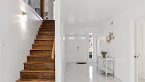 A staircase with wooden steps leading to a white interior space with a marble floor and a white console table with a plant. - Corpus Christi Gem (Corpus Christi)