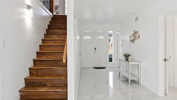 A staircase with wooden steps leading to a white interior space with a marble floor and a white console table with a plant.